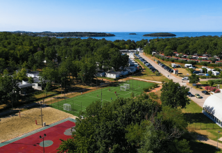 Luftfoto af Camping Bijela Uvala i Istrien, Kroatien med sportsbaner, campingvogne og udsigt til havet.