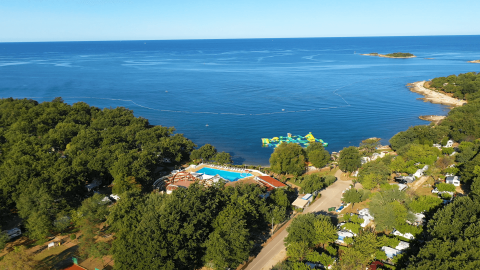 Vista aérea de Camping Bijela Uvala en Istria, Croacia con piscina, árboles y parque acuático flotante en el mar.