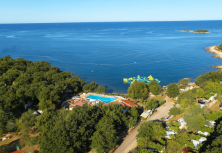 Vista aerea di Camping Bijela Uvala in Istria, Croazia, con piscina, alberi e parco acquatico galleggiante sul mare.