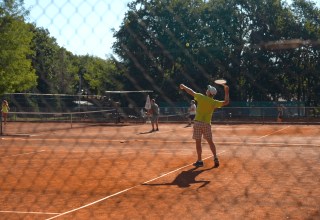 Folk spiller tennis på en rød grusbane omgivet af træer hos Camping Bijela Uvala i Istrien, Kroatien.