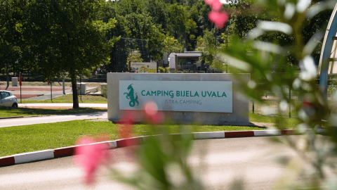 Entrada a Camping Bijela Uvala, un parque vacacional en Istria, Croacia, rodeado de árboles y césped.