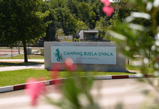 Indgangen til Camping Bijela Uvala, en feriepark i Istrien, Kroatien, med et skilt og grønne træer.