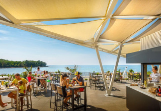 Udendørs restaurant ved Camping Aminess Maravea i Istrien, Kroatien, med havudsigt og afslappede gæster.