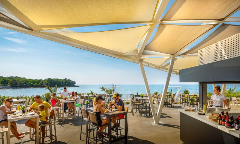 Restaurant extérieur au Camping Aminess Maravea en Istrie, Croatie, vue sur mer et clients détendus.