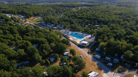 Vista aérea de Camping Bijela Uvala en Istria, Croacia, con piscina, casas rodantes y árboles frondosos.