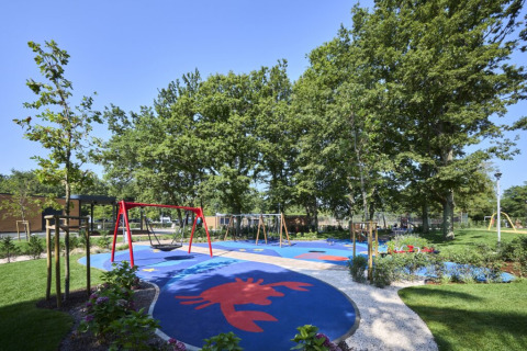 Spielplatz mit Schaukeln und buntem Bodenbelag inmitten von Bäumen im Camping Bijela Uvala in Istrien, Kroatien.