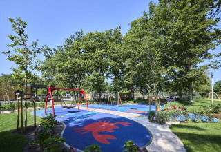 Parco giochi con altalene e pavimento colorato tra alberi presso Camping Bijela Uvala, Istria, Croazia.