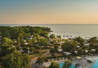 Campeggio Aminess Maravea in Istria, Croazia, con caravan, piscina, vegetazione e vista mare al tramonto.