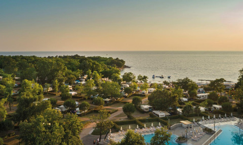 Camping Aminess Maravea en Istrie, Croatie, avec caravanes, piscine, verdure luxuriante et vue sur la mer au coucher du soleil.