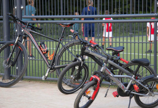 Deux vélos appuyés contre une barrière devant un terrain de foot à hu Birkelt Village, Mersch, Luxembourg.