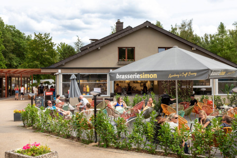 Caffè all'aperto al villaggio hu Birkelt di Mersch, Lussemburgo, con persone sedute sotto gli ombrelloni.