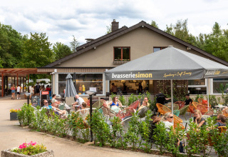 Udendørs café i hu Birkelt Village feriepark, Mersch, Luxembourg, med folk under store parasoller.
