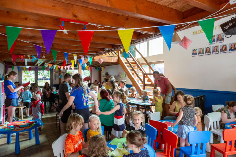 Children and adults join craft activities under colorful bunting in a busy hall at hu Birkelt Village, Luxembourg.