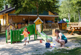 Børn leger på legeplads med voksen i hu Birkelt Village feriepark, Mersch, Luxembourg, på en solrig dag.