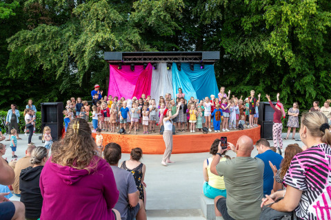 Children and adults enjoy a staged activity at a holiday park in Mersch, Luxembourg, surrounded by trees.