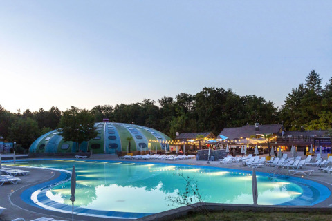 Piscina al atardecer en el parque vacacional hu Birkelt Village en Mersch, Luxemburgo, rodeada de árboles y luces.