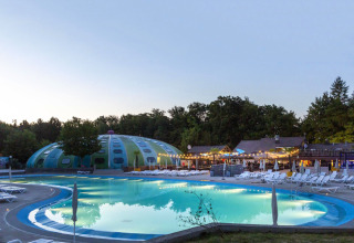 Piscina al atardecer en el parque vacacional hu Birkelt Village en Mersch, Luxemburgo, rodeada de árboles y luces.