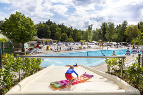 Niño en tobogán acuático con flotador en una piscina al aire libre en hu Birkelt Village, Luxemburgo.