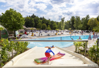 Child on a waterslide with an inflatable float at an outdoor pool in hu Birkelt Village, Luxembourg.