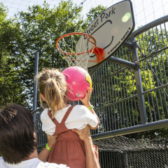 Un adulto ayuda a una niña a lanzar una pelota rosa en una canasta de baloncesto en hu Birkelt Village, Mersch.
