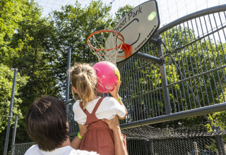 Un adulto ayuda a una niña a lanzar una pelota rosa en una canasta de baloncesto en hu Birkelt Village, Mersch.