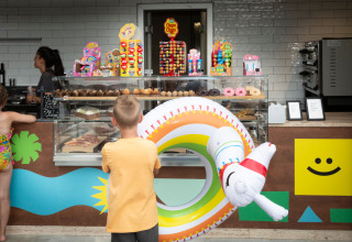 Børn i badetøj bestiller bagværk og slik i en farverig café ved hu Birkelt Village, Luxembourg.