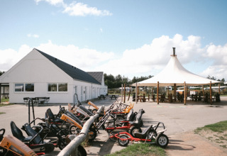Billedet viser Løkken Klit Camping i Nordjylland med cykelbiler, en hvid bygning og et stort telt.