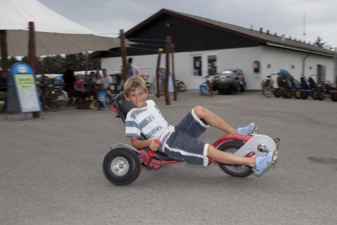 Niño conduciendo un triciclo frente a un parque vacacional en Løkken Klit Camping, Jutlandia del Norte, Dinamarca.