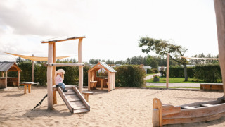 Holzspielplatz mit Sand und kleinen Hütten im Løkken Klit Camping in Nordjütland, Dänemark, bei Tageslicht.