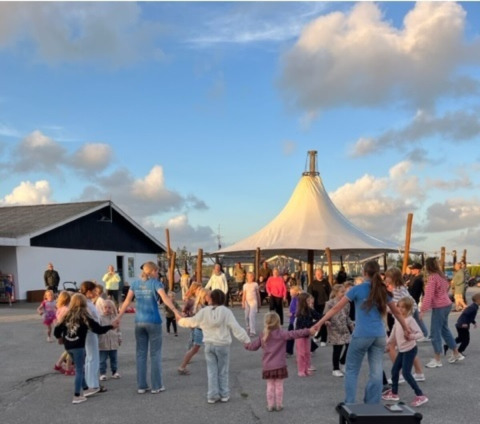 Kinderen en volwassenen dansen in cirkel op Løkken Klit Camping, Noord-Jutland, Denemarken.