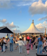 Kinder und Erwachsene tanzen im Kreis bei Løkken Klit Camping bei sonnigem Himmel in Nordjütland, Dänemark.
