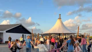 Kinder und Erwachsene tanzen im Kreis bei Løkken Klit Camping bei sonnigem Himmel in Nordjütland, Dänemark.