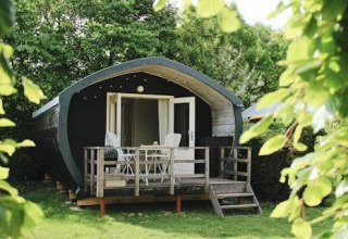 Wooden cabin with porch at 7Huizen aan Zee holiday park, nestled among green trees in Zeeland, Netherlands.
