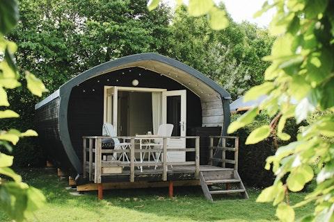 Wooden cabin with porch at 7Huizen aan Zee holiday park, nestled among green trees in Zeeland, Netherlands.