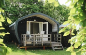 Wooden cabin with porch at 7Huizen aan Zee holiday park, nestled among green trees in Zeeland, Netherlands.