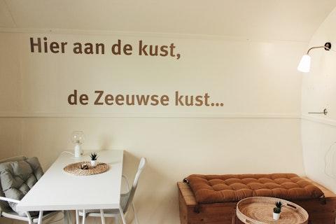 Knusse zithoek bij 7Huizen aan Zee, Zeeland, met Nederlandse tekst op de muur als decoratie.