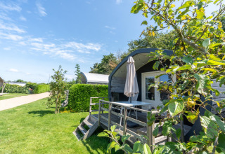 Feriehytte med terrasse og parasol i grønne omgivelser på 7Huizen aan Zee feriepark i Zeeland, Holland.
