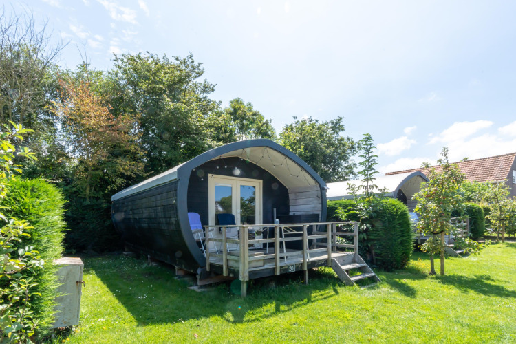 Holiday cabin with terrace and chairs surrounded by greenery at 7Huizen aan Zee holiday park in Zeeland, Netherlands.