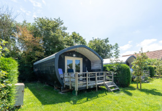 Feriehytte med terrasse og stole omgivet af grønt område ved 7Huizen aan Zee feriepark, Zeeland, Holland.