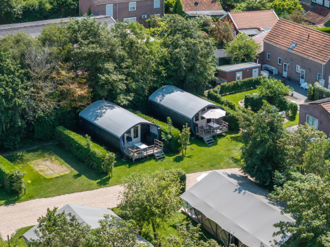 Luchtfoto van moderne hutten en tenten in het groen van vakantiepark 7Huizen aan Zee in Zeeland.