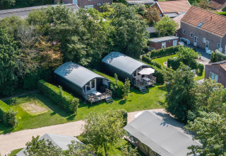 Luftfoto af to moderne hytter og telte i grønne omgivelser ved 7Huizen aan Zee feriepark i Zeeland.