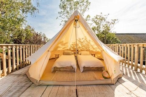 Tienda glamping con dos camas individuales en terraza de madera en 7Huizen aan Zee, parque en Zelanda, Países Bajos.