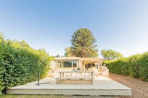Holiday home with wooden deck, picnic table, and lush hedges at 7Huizen aan Zee holiday park in Zeeland.
