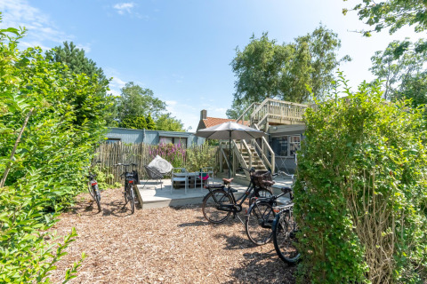 Außenterrasse mit Fahrrädern, Tischen, Stühlen und Sonnenschirm im 7Huizen aan Zee Ferienpark in Zeeland, Niederlande.