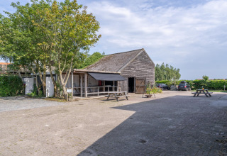Image of rustic barn and courtyard with picnic tables at 7Huizen aan Zee holiday park in Zeeland, Netherlands.