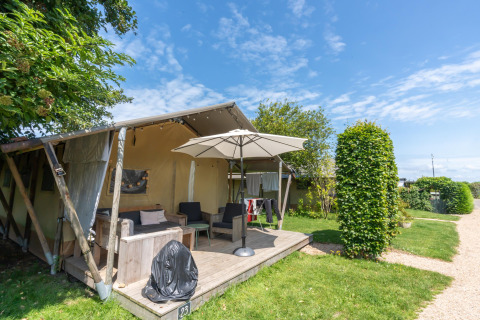 Feriehytte med overdækket terrasse og parasol ved 7Huizen aan Zee feriepark i Zeeland, Holland, på en solskinsdag.