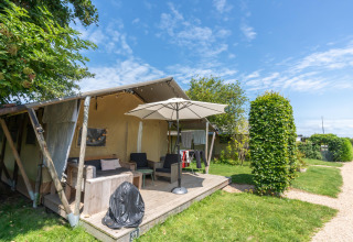 Feriehytte med overdækket terrasse og parasol ved 7Huizen aan Zee feriepark i Zeeland, Holland, på en solskinsdag.