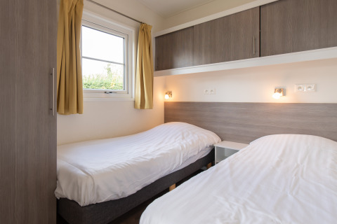 Lichte kamer met twee éénpersoonsbedden, gele gordijnen en moderne kasten in Comfort Lodge, Kompas Camping Nieuwpoort.