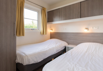 Lichte kamer met twee éénpersoonsbedden, gele gordijnen en moderne kasten in Comfort Lodge, Kompas Camping Nieuwpoort.