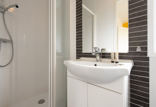 Modernes Badezimmer im Comfort Lodge Tiny House auf dem Kompas Camping Nieuwpoort, Belgien, mit Dusche und Waschbecken.